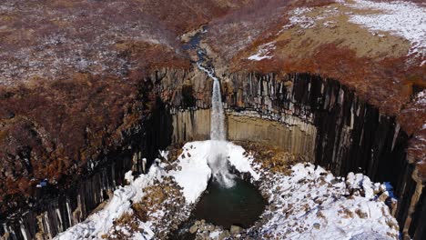 Small-Waterfall-cascades-into-frozen-lake,-geological-formation-after-eruption