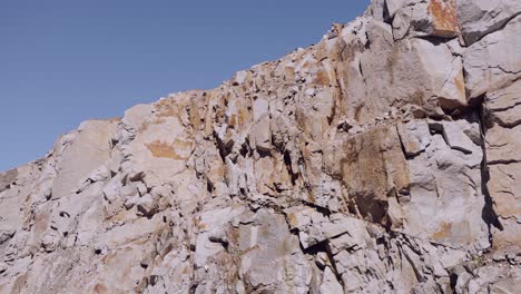 Schroffe-Felswand-Mit-Detaillierten-Felsstrukturen-Unter-Klarem-Blauen-Himmel