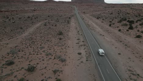 Aerial-of-a-camper-van-as-it-traverses-the-desert-road-within-Monument-Valley-Park,-Utah,-USA,-embodying-the-spirit-of-van-life,-travel,-and-exploration