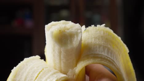 Bitten-and-peeled-banana-against-a-blurred-background,-held-in-someone-hand