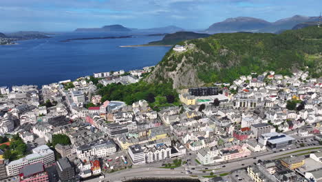 Drone-Aerial-View-of-Alesund,-Norway-on-Sunny-Summer-Day,-Town-Buildings,-Hill-With-Viewpoint-and-Islands-in-Bay