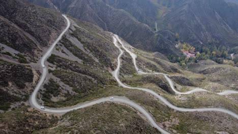 Aerial-view:-Vehicles-ascend-gravel-road-switchbacks-up-mountain-slope