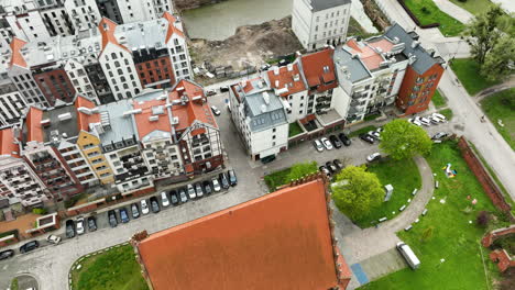 Diagonal-aerial-view-of-a-dense-urban-area-in-Elbląg-with-a-mix-of-colorful-buildings,-parked-cars,-and-a-patch-of-green-space
