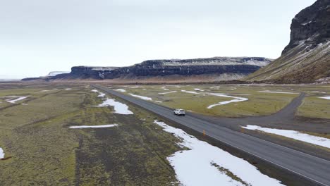 Panoramic-Drone-Follows-White-Van-Driving-Through-Icelandic-Mountains-Landscape