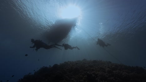 Gegenlichtaufnahme-Von-Tauchern-Unter-Einem-Tauchboot-Im-Klaren,-Blauen-Wasser-Neben-Einer-Tropischen-Korallenriff-Silhouette,-Schönheitsaufnahme-Auf-Der-Insel-Tahiti,-Französisch-Polynesien