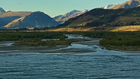 Panorámica-Aérea-Sobre-El-Lago-Wakatipu-Y-El-Punto-De-Encuentro-Del-Río-Mientras-La-Luz-Del-Sol-Se-Rompe-Entre-Las-Nubes-En-La-Distancia