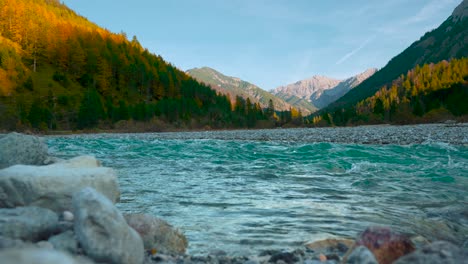 Clear-blue-mountain-river-water-rushing-by-scenic-colorful-autumn-trees-in-the-evening-sun,-Austrian-alps