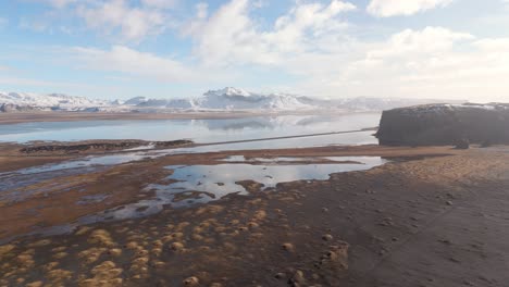 Volcanic-soil-formation-around-snowy-mountains-Icelandic-lake,-drone,-sunny-day