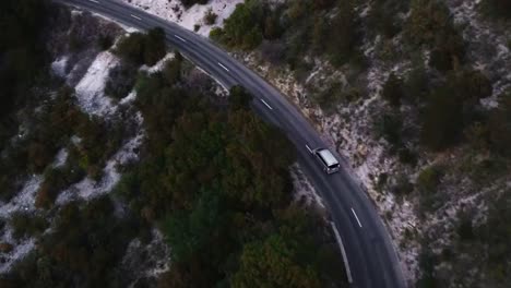 Aerial-of-a-car-gracefully-traverses-a-winding-road-nestled-amidst-mountains,-embodying-the-spirit-of-adventure,-freedom,-and-exploration-amidst-breathtaking