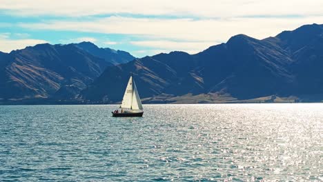 Sunlight-glistens-on-Lake-Hawea-as-group-sails-across-in-front-of-steep-mountains