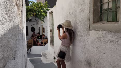 Female-tourist-taking-a-picture-on-a-small-alley-in-Santorini,-Greece