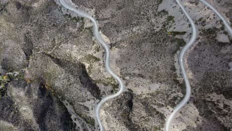 Aerial:-Lone-car-climbs-arid-mountain-pass-on-gravel-road-switchback