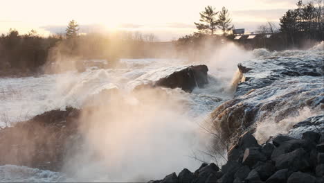 A-powerful-river-cascades-over-a-rocky-outcrop,-its-mist-illuminated-by-a-fiery-sunset