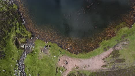 Aerial-view-of-two-hikers-sat-at-Blueberry-Tarn,-Lake-District---UK