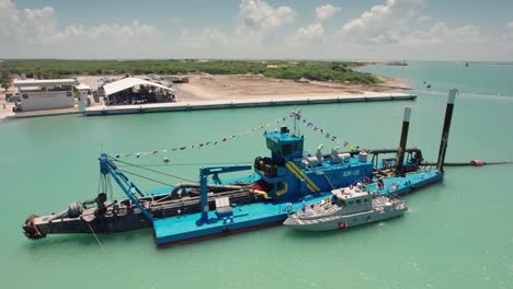 Drone-approaching-a-sand-dredger-boat-and-lifting-to-reveal-a-sand-extraction-plant