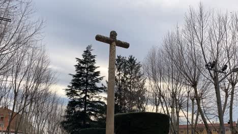 filming-of-a-granite-stone-cross-with-its-pedestal-with-inscriptions-located-in-the-surroundings-of-the-church-of-San-Nicolas-with-the-background-of-a-park-with-trees-on-a-winter-morning