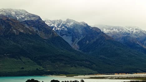 Mist-falls-on-snow-dusted-mountain-landscape-overlooking-glacial-river,-Glenorchy