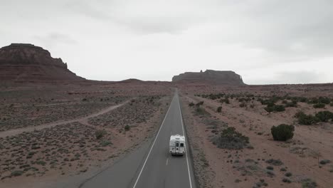 Tracking-aerial-view-of-a-camper-van-journeying-along-the-desert-road-in-Monument-Valley-Park,-Utah,-USA,-encapsulating-the-essence-of-van-life,-travel,-and-exploration