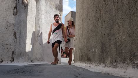Loving-couple-holding-hands-and-walking-in-small-alley-in-santorini,-Greece