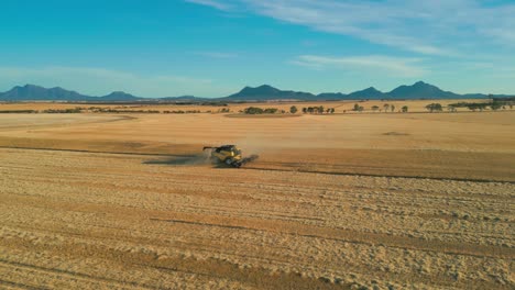 aerial-view-over-wheat-field-and-a-combine-harvester-with-the-stirling-range-national-park-in-the-background,-western-australia
