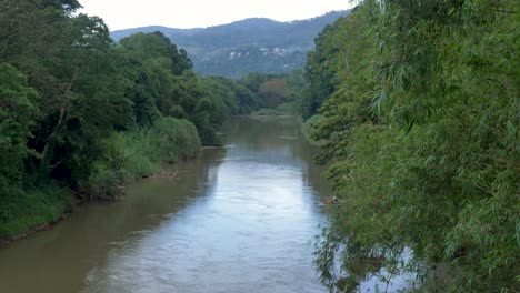 Slow-motion-SLR-landscape-view-of-Mahaweli-Ganga-Kandy-river-water-stream-flowing-surrounding-by-trees-in-Botanical-gardens-Sri-Lanka-Asia-travel-nature