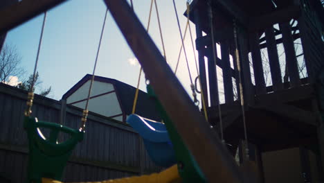 Purple-anamorphic-sun-flare-peeks-out-behind-a-swingset-and-wooden-play-structure-in-a-backyard-in-slow-motion