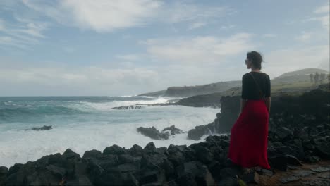 Woman-in-a-red-dress,-enjoying-sun-and-ocean-at-rocky-Playa-de-las-Americas-beach-in-Tenerife