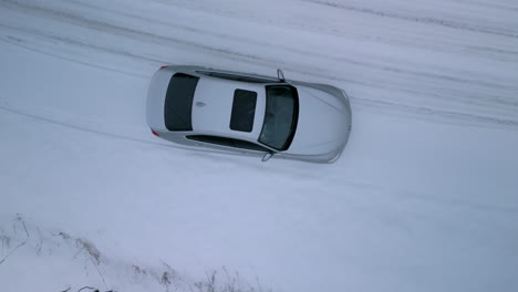 Eine-Luftaufnahme-Einer-Drohne,-Die-Auf-Ein-Auto-Herabsteigt,-Das-Entlang-Einer-Verschneiten-Landstraße-Im-Winter-Geparkt-Ist