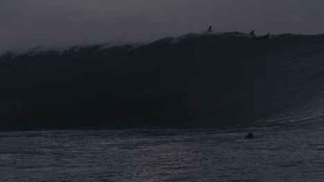 Perfect-big-wave-breaks-across-surfers-at-dusk-in-slow-motion