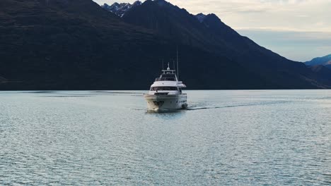 Frontale-Luftaufnahmen-Nach-Hinten,-Während-Eine-Yacht-Unter-Epischen-Bergen-In-Neuseeland-Hindurchfährt