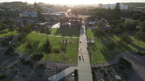 Aerial-tracking-shot-of-person-jogging-on-path-in-park-during-golden-sunset