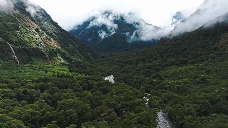 Aerial-pullback-establishes-tropical-valley-covered-with-thick-clouds-on-peaks,-Milford-Sound-NZ