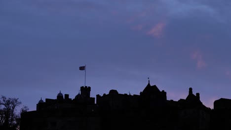 Silhouette-of-Edinburgh-Castle-with-Union-Jack-Flag-at-sunset-on-a-winter's-night,-Scotland