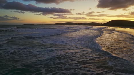 Golden-hour-dusk-glow-lights-up-sky-reflecting-on-whitewash-wave-texture-in-ocean