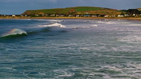 Waves-roll-and-crash-along-shallow-waters-in-Curio-Bay-with-village-behind