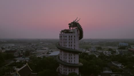 Embrace-the-enchanting-beauty-of-Bangkok's-Wat-Samphran-Temple-as-the-sun-sets-behind-its-iconic-dragon-building,-captured-in-detail-by-drone-footage