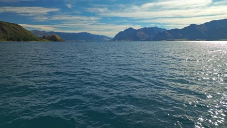 Aerial-dolly-above-shining-sparkling-water-of-Lake-Hawea-on-beautiful-summer-day