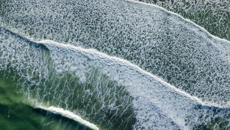 Drone-top-down-aerial-green-water-texture-of-crashing-waves-with-ripples-in-whitewash