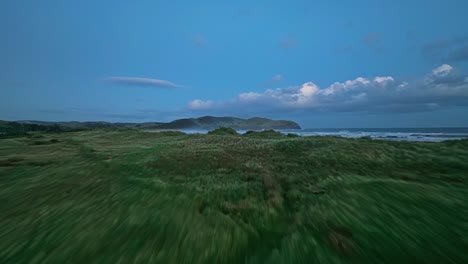 Aerial-dolly-above-grassland-paths-rises-to-establish-rolling-waves-along-shoreline