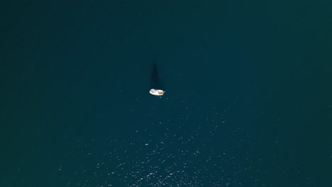 Drone-top-down-overview-of-sailboat-and-sail-shadow-across-dark-waters