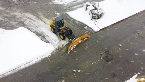 Snow-plow-cleaning-the-streets-covered-in-snow-supermarket-car-park-aerial