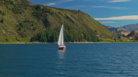 órbita-Aérea-Baja-Alrededor-De-Un-Velero-Deslizándose-A-Través-Del-Lago-Hawea-Reflejando-Una-Vela-Blanca-En-El-Agua