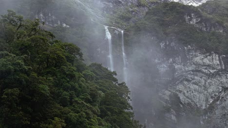 Mist-floats-in-front-of-cascading-waterfall-over-tropical-forest-in-New-Zealand