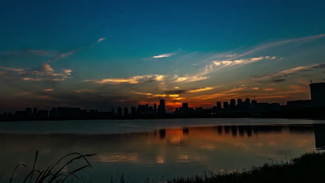 Zeitraffer-Silhouetten-Mit-Farbenfrohem-Sonnenuntergang-über-Einem-Kleinen-See-In-Der-Nähe-Der-Stadt,-Sommerabend-Video