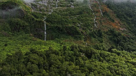 Gentle-cascading-waterfalls-descend-on-steep-escarpment-of-the-lush-forests-below-clouds