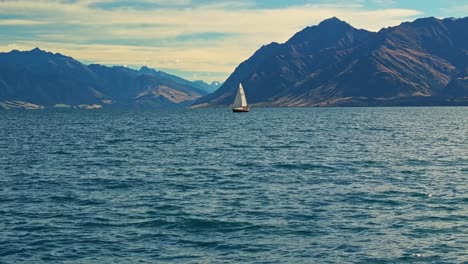 Drone-tilt-up-establishes-sailboat-floating-calmly-on-waters-of-Lake-Hawea
