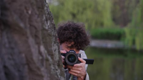 Paparazzi-detective-hide-behind-tree-trunk-and-use-digital-camera-to-take-photos