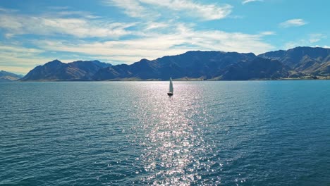 Aerial-pullback-as-sailboat-sits-in-middle-of-sun-ray-reflecting-sparkling-on-water