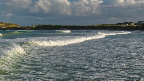 Low-aerial-tracking-pan-follows-waves-breaking,-ocean-water-texture-below-low-cliffs