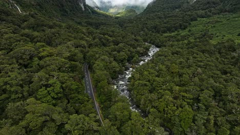 Aerial-dolly-above-road-snaking-following-rocky-river-at-valley-base-in-Milford-Sound